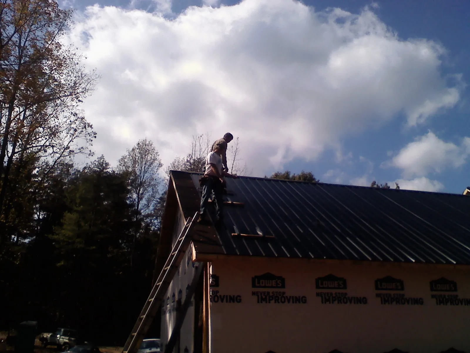 Roofer fastening dark metal panels high against a cloudy sky, from a Roof Inspection job in Decatur
